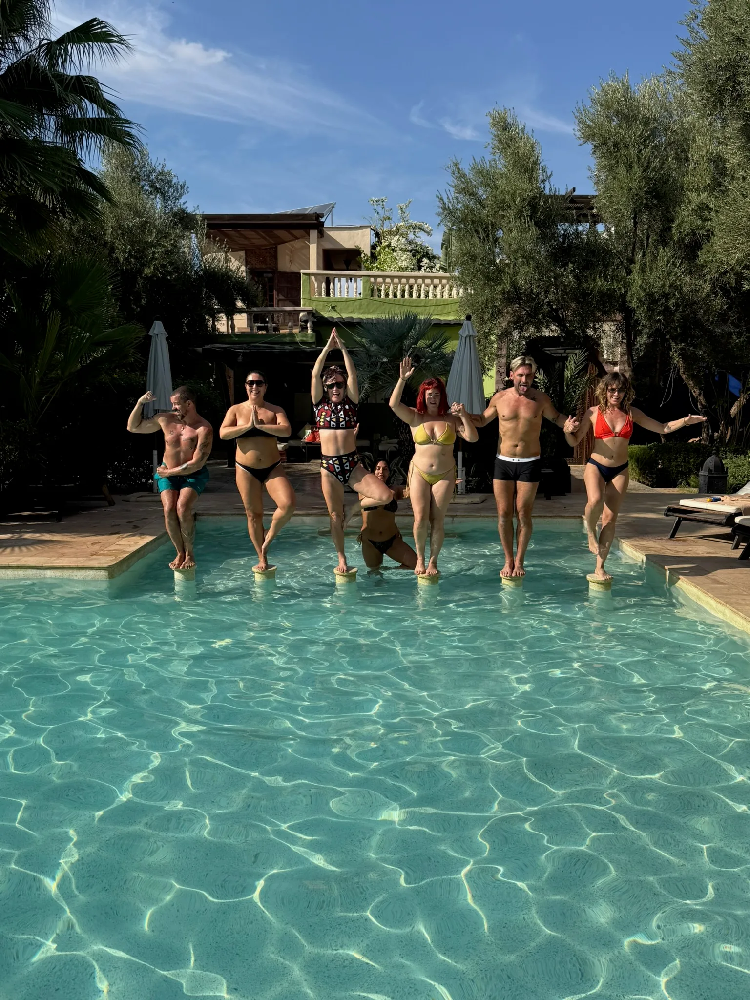 Retreat guests in tree pose on stepping stones in the pool in Marrakesh